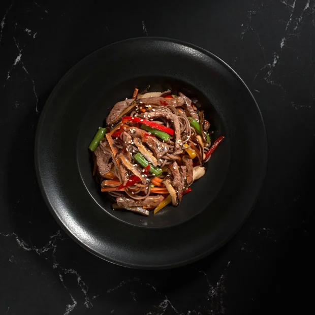 Sliced beef and buckwheat noodles with peppers on a black plate