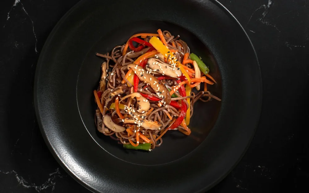 Stir-fried noodles with peppers, carrots and mushrooms on a black plate